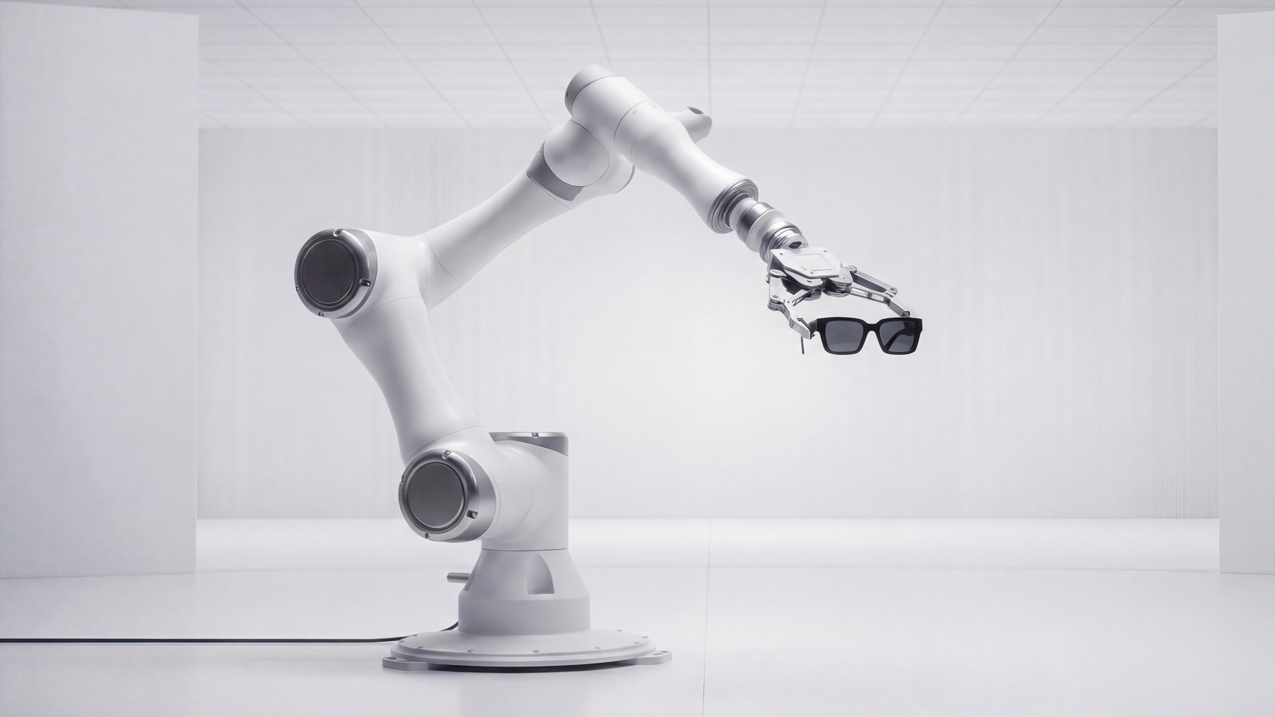 Braccio robotico che regge un paio di occhiali da sole in uno studio bianco, con il logo Ottica Vicari in filigrana sullo sfondo
